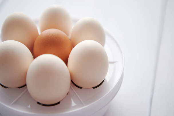 Курячі яйця в яєчній електричній плиті на білому дерев'яному столі
 - Фото, зображення