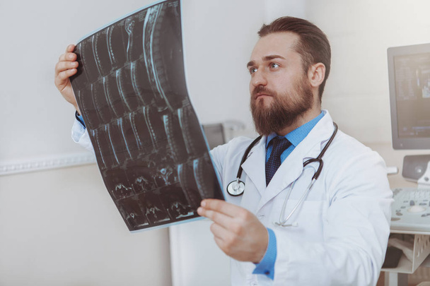 Врач-мужчина осматривает рентген в своем кабинете
 - Фото, изображение