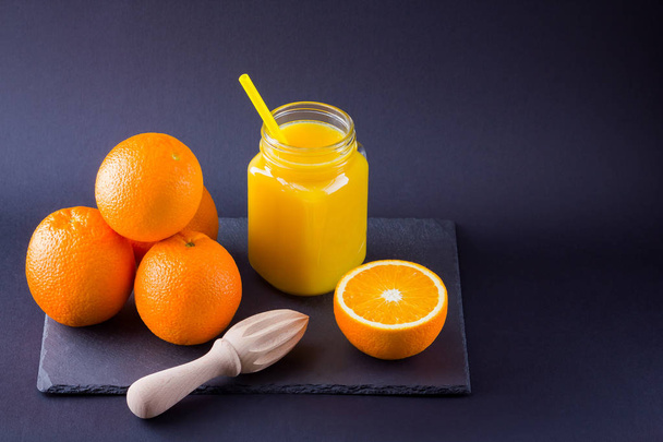 Orange fruits and juice on black background. Citrus fruit for making juice with manual juicer. Oranges on slate board. Mason jar with orange juice. Copy space - Foto, afbeelding