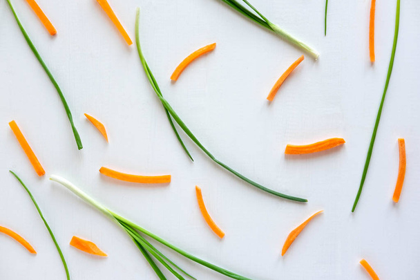Pattern with green onions and carrot slices on a white wooden background. Kitchen Pattern. View from above - Фото, изображение