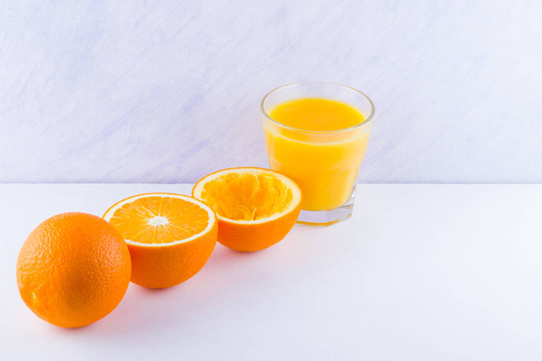 Orange fruits with juice, concept. Orange juice and halves of oranges on white background. Citrus for making juice. Whole and squeezed oranges and glass of juice - Photo, image