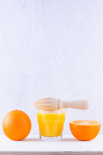 Orange fruits with juice, concept. Orange juice and halves of oranges on white background. Citrus for making juice and manual juicer. Whole and squeezed oranges and glass of juice - Фото, изображение