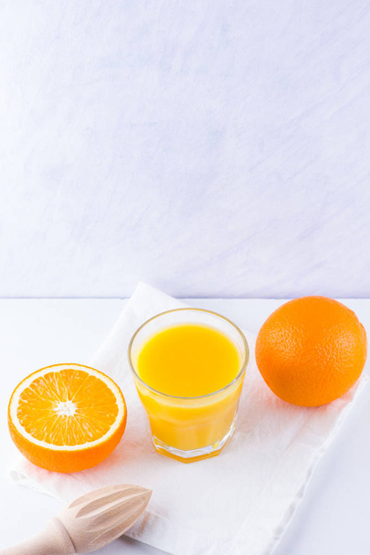 Orange fruits with juice, concept. Orange juice and halves of oranges on white background. Citrus for making juice and manual juicer. Whole and squeezed oranges and glass of juice - 写真・画像