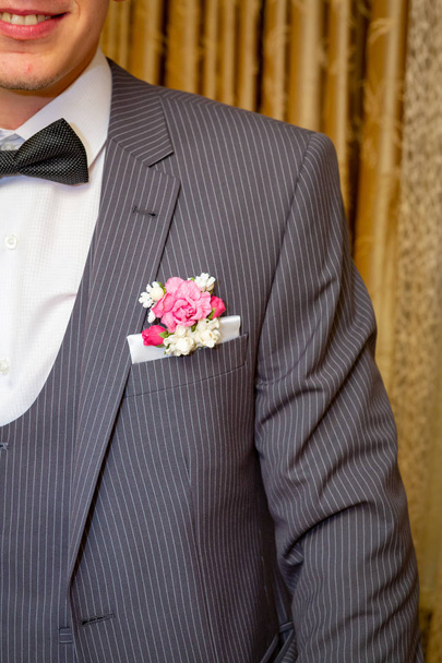 The groom in a gray pinstripe suit, white shirt with black bow tie, with flowers in his jacket pocket. - Photo, Image
