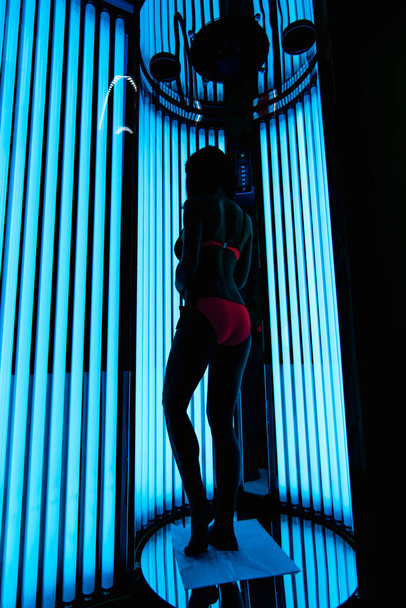 girl in the vertical Solarium. Silhouette on the background of ultraviolet lamps - Fotó, kép
