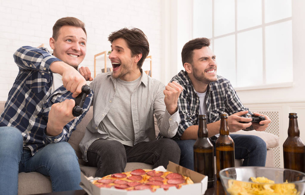 Авидийские геймеры. Возбужденные мужчины играют в видеоигры дома
 - Фото, изображение