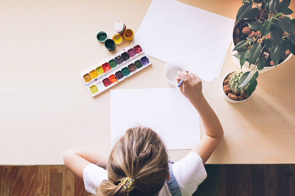 Дівчинка малює кольоровими фарбами на білому папері за столом. Вид зверху. Копіювати простір
 - Фото, зображення