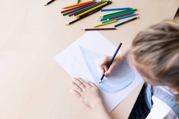 Una niña dibuja una gota de agua azul pura con lápices de colores. Concepto de ecología y protección del medio ambiente
 - Foto, Imagen