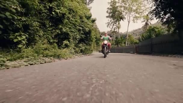 Man motorcyclist driving on motorbike on countryside road on palm trees background. Senior motorcycle rider driving on motorcycle. Moto travel concept. - Materiał filmowy, wideo