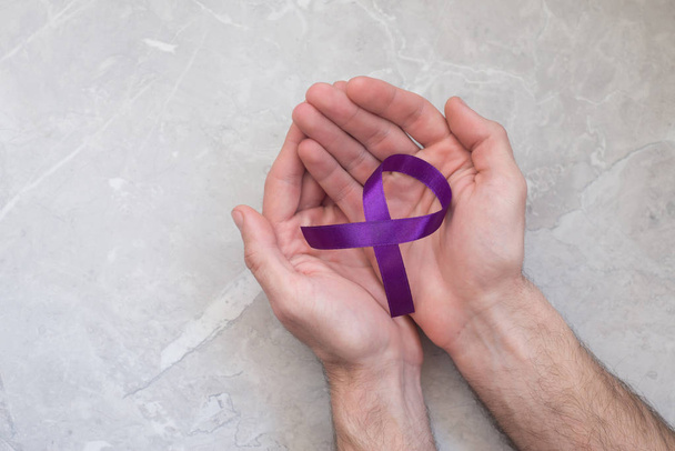 Hombre sosteniendo cinta de cáncer violeta, símbolo del páncreas. Concepto de salud y medicina
.  - Foto, Imagen