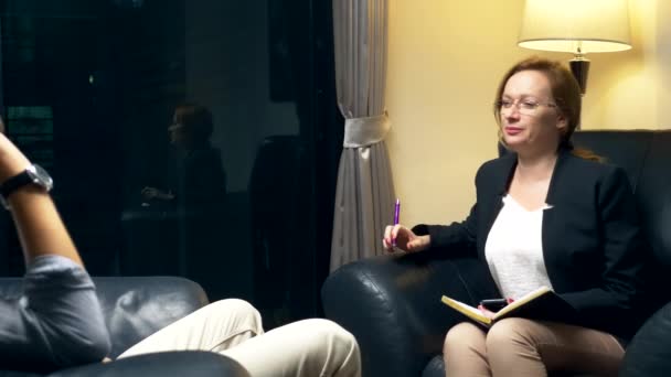 concept of negotiation, psychological counseling. A woman with a notebook communicates with a successful man. sitting in the evening in the office in a leather chair. - Záběry, video