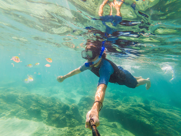 fiatal férfiak snorkeling feltárása víz alatti korallzátony táj háttérben a mély kék óceán színes hal és a tengeri élet - Fotó, kép