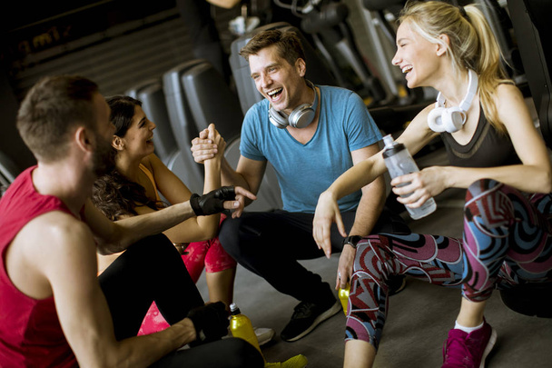 Grupa PF młodych ludzi w odzieży sportowej rozmowy i śmiech razem podczas odpoczynku w siłowni po treningu - Zdjęcie, obraz