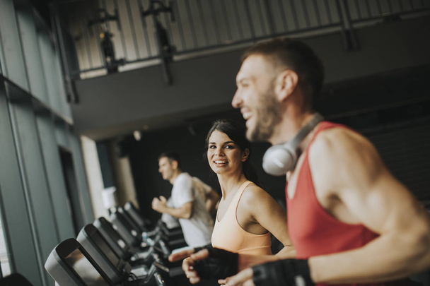 Νεαρό ζευγάρι τρέχει επάνω treadmills στο σύγχρονο γυμναστήριο - Φωτογραφία, εικόνα