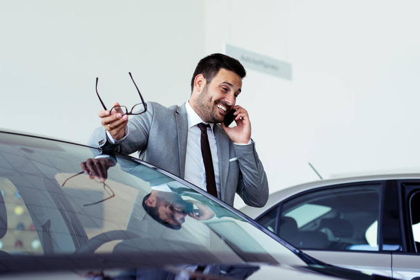Businessman having a phone call at the car showroom  - Фото, изображение