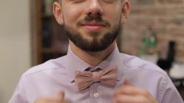 Groom adjusts bow tie in barbershop background. Preparing to go to the bride - Footage, Video