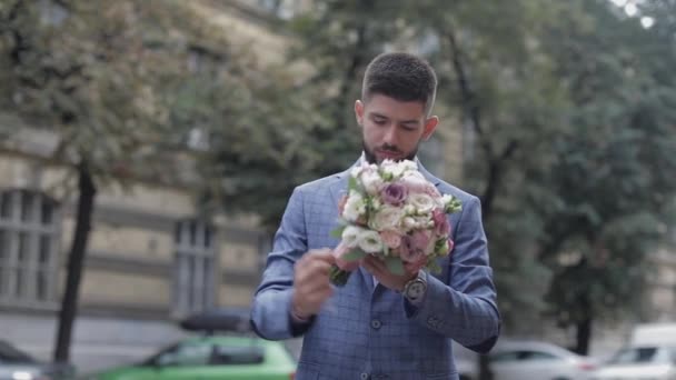 Groom with a black beard with wedding bouquet on the street. Wedding day - Záběry, video
