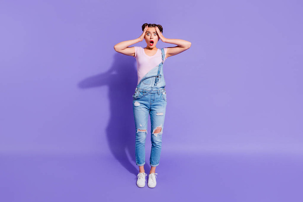 Full length body size photo yelling beautiful she her lady two buns hands arms hold head oh no expression wear casual t-shirt jeans denim overalls outfit isolated purple violet bright background - Foto, immagini