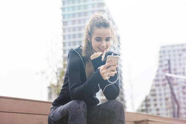 Χαμογελαστή νεαρή γυναίκα με smartphone και ακουστικά ακούγοντας μουσική υπαίθρια - Φωτογραφία, εικόνα