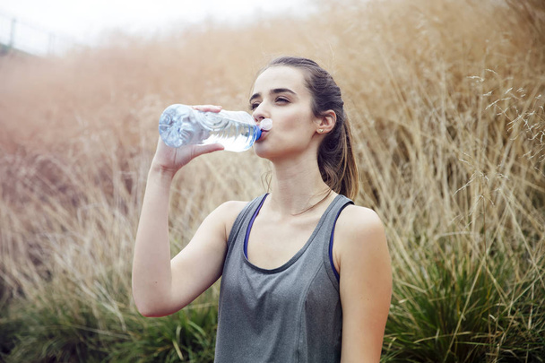 Mujer joven sentada en el parque y bebiendo agua después del ejercicio
 - Foto, imagen