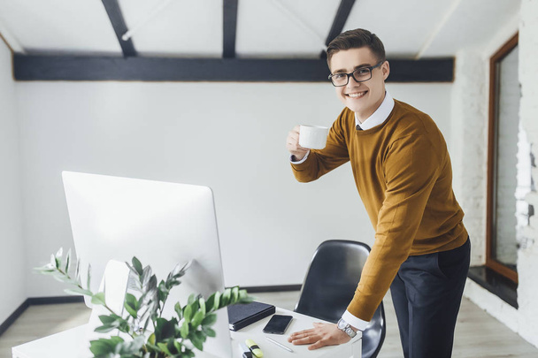 Attractive young businessman with cup of coffee working at office  - Foto, afbeelding