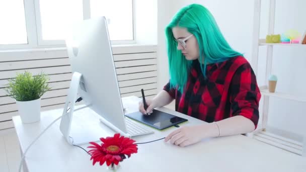 Młody projektant graficzny z kolorową fryzurą pracując na komputerze za pomocą tabletu - Materiał filmowy, wideo