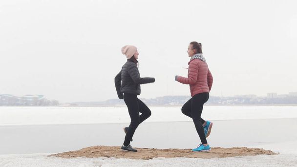 zwei athletische Frauen laufen auf der Stelle an einem verschneiten Strand - Foto, Bild