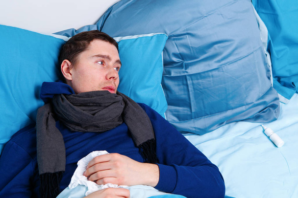 Bild eines kranken Mannes in Schal und mit Taschentüchern im Bett liegend. - Foto, Bild