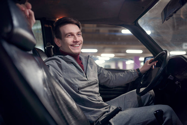 Εικόνα από την πλευρά του ευτυχισμένο άνθρωπο κοιτάζοντας την κάμερα κάθεται στο αυτοκίνητο. - Φωτογραφία, εικόνα