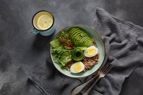 Vegan Buddha bowl with buckwheat, avocado, boiled eggs, cucumber, arugula beet leaves. Diet, detox, healthy food concept  - Zdjęcie, obraz