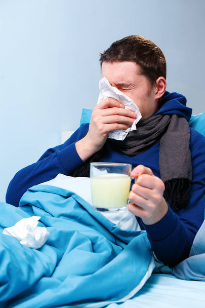 Foto de hombre enfermo en bufanda con taza de medicina acostado en la cama
 - Foto, imagen