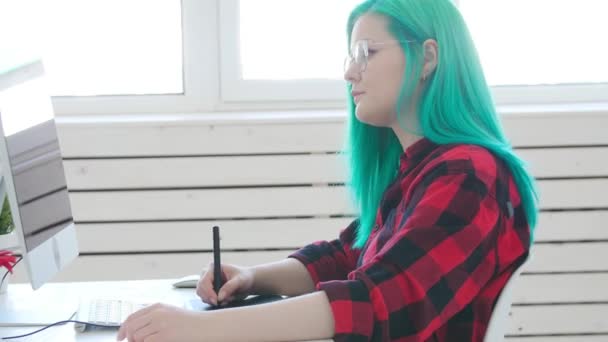 Jovem designer gráfico com cabelos coloridos trabalhando no computador usando tablet
 - Filmagem, Vídeo