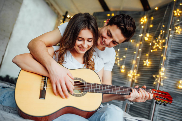 Handsome young man teaching woman playing acoustic guitar at home  - Photo, image