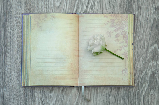 Kis fehér Rózsa fekszik a szüreti napló a háttérben egy szürke fából készült asztal. - Fotó, kép