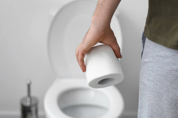 Человек с рулоном туалетной бумаги в туалете, крупным планом
 - Фото, изображение