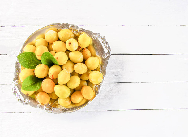 Ciruelas amarillas frescas. Frutos maduros en un plato sobre fondo de tablas blancas
. - Foto, Imagen