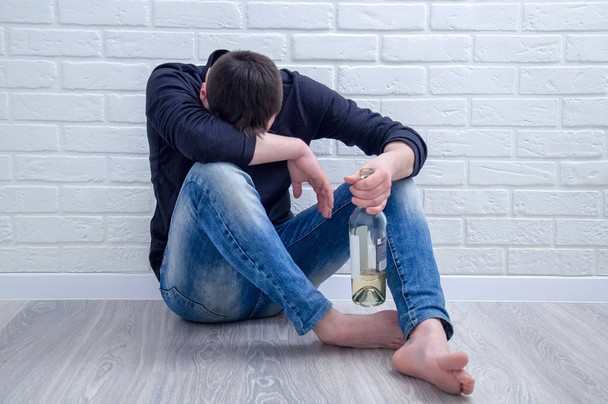 Depressed young man drinking wine alone.  Depressive guy drinks alcohol. - Фото, изображение