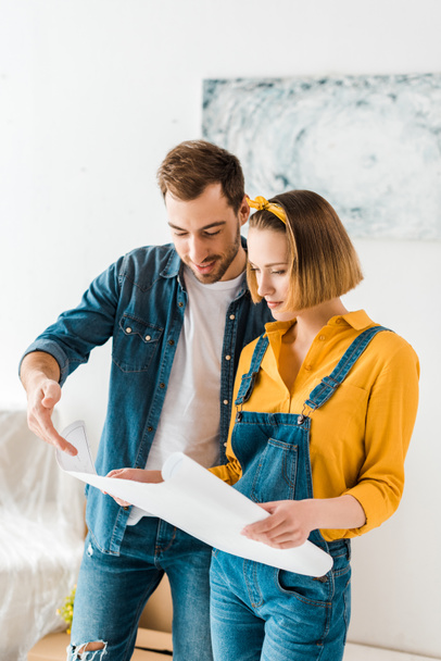 cheerful couple in jeans looking at blueprint at home - Fotoğraf, Görsel