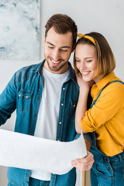 cheerful couple in jeans looking at blueprint at home - Foto, immagini
