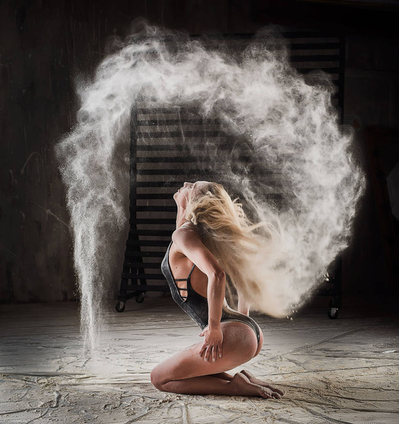 Beautiful blonde dancing in clouds of flour. Woman throws flour into the air. - Фото, изображение