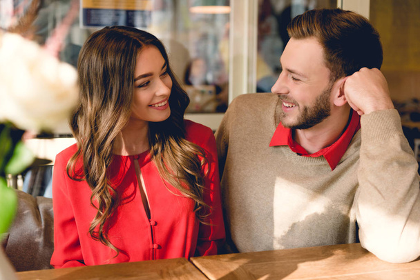 handsome bearded man smiling while looking at beautiful girl in cafe  - Foto, imagen