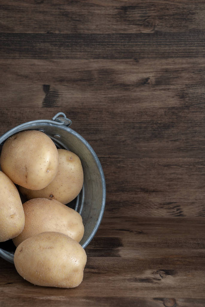 Close-up on vertical of potatoes in metal bucket on dark wooden background - Foto, Bild