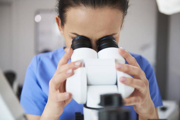 Εστιασμένος οδοντίατρος κοιτάζοντας μέσα από το μικροσκόπιο  - Φωτογραφία, εικόνα