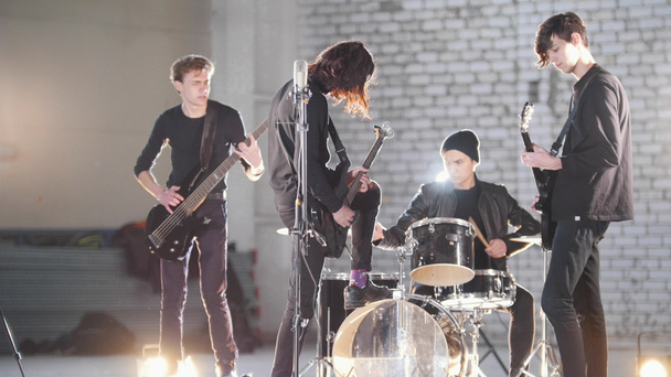 eine junge Rockgruppe bei einer Wiederholung in einem Hangar. Mitglieder einer Gruppe in schwarzer Kleidung. helle Beleuchtung - Foto, Bild