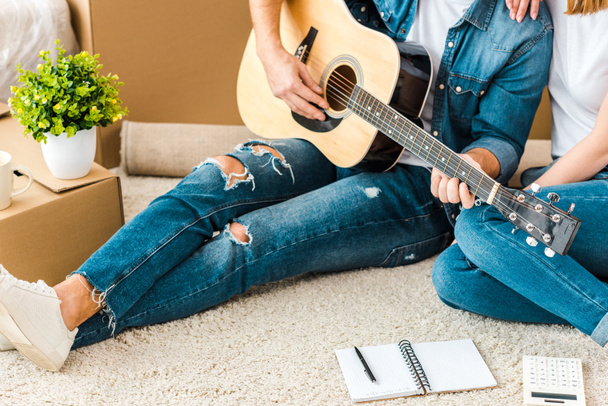 Wykadrowany widok człowieka siedzącego na dywanie z żoną i grając na gitarze akustycznej - Zdjęcie, obraz