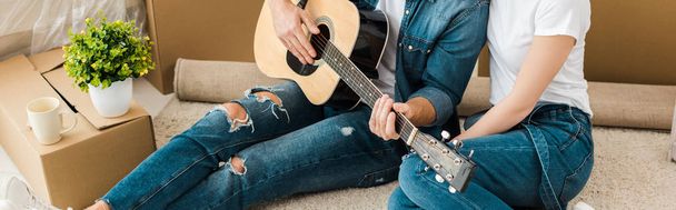 Panoramic shot of man sitting on carpet with wife and playing acoustic guitar - Photo, Image