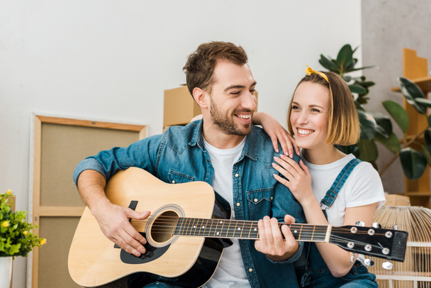 sonriente hombre tocando la guitarra acústica a esposa en casa
 - Foto, Imagen