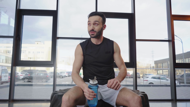 Spor şişeyi açan Beyaz şortlu Sportsman, içme suyu, alnını silerek ve kameraya gülümsüyor - Video, Çekim