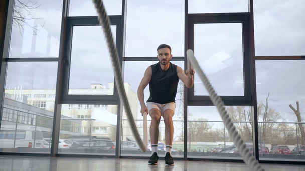 Vista frontal do desportista concentrado fazendo exercício com cordas no ginásio
 - Filmagem, Vídeo