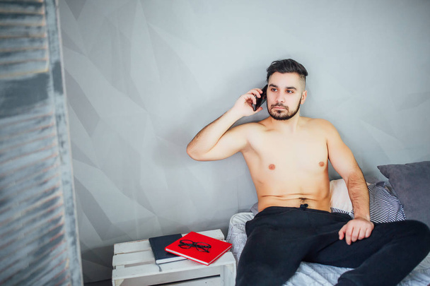 Young man lying on bed and talking on smartphone - Zdjęcie, obraz